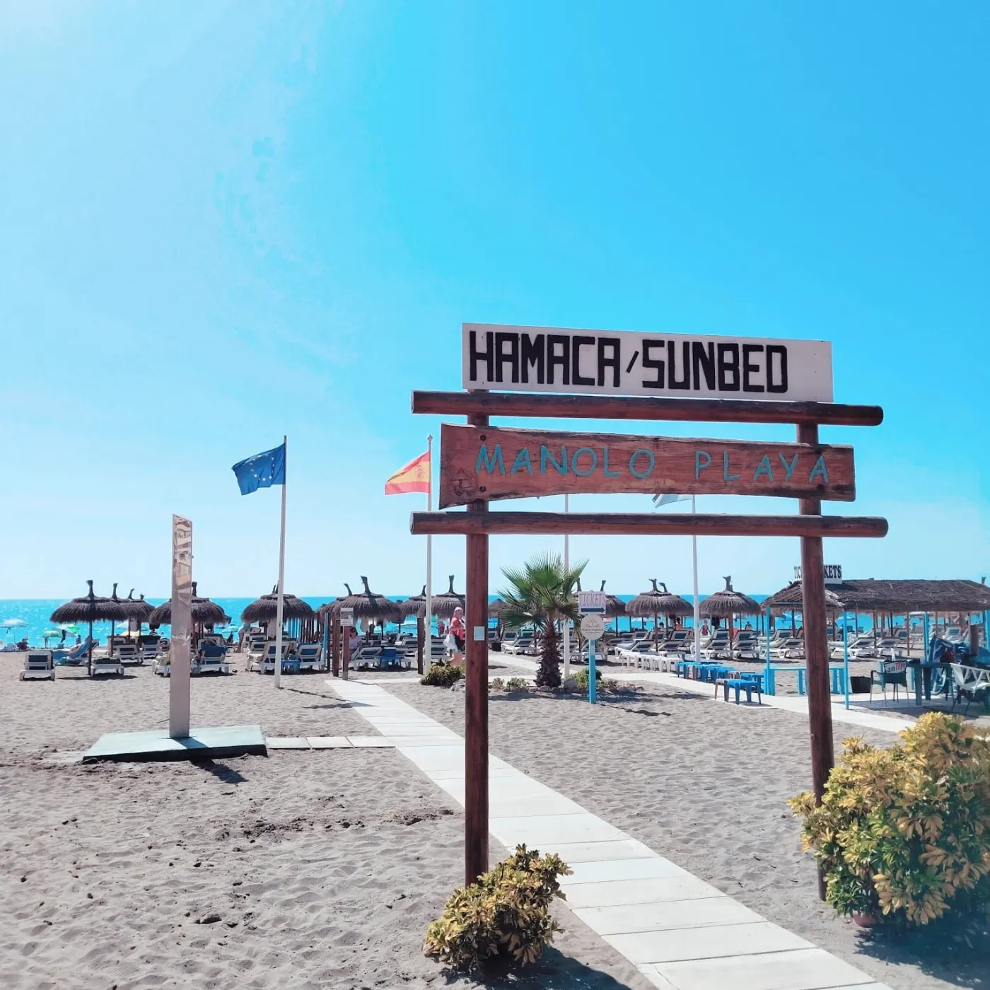 Cartel de madera de Playa Manolo que dice Hamaca / Sunbed, a la entrada de la playa